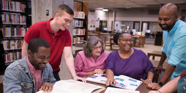 A diverse group of people in the library around a table.