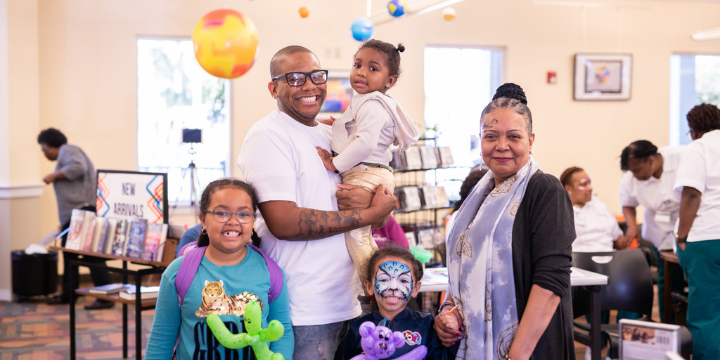 Two parents and their three children enjoying an in-person event where they enjoyed face paining and were giving balloon animals.