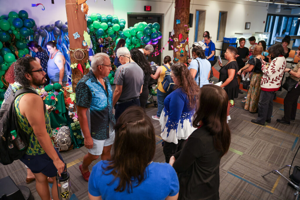 Crowd shot of people admiring a soft sculpture installation of crochet, knits and sewn projects with balloon sculpture in t he background