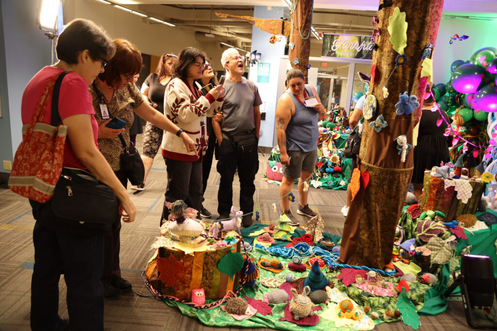 Crowd shot of people admiring a soft sculpture installation of crochet, knits and sewn projects