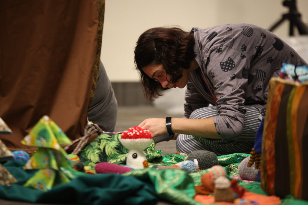 Woman sitting on the floor arranging soft sculpture elements in an enchanted forest theme