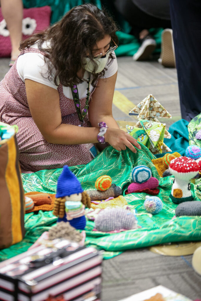 Woman sitting on the floor attaching soft sculpture trees to green fabric meant to represent grass