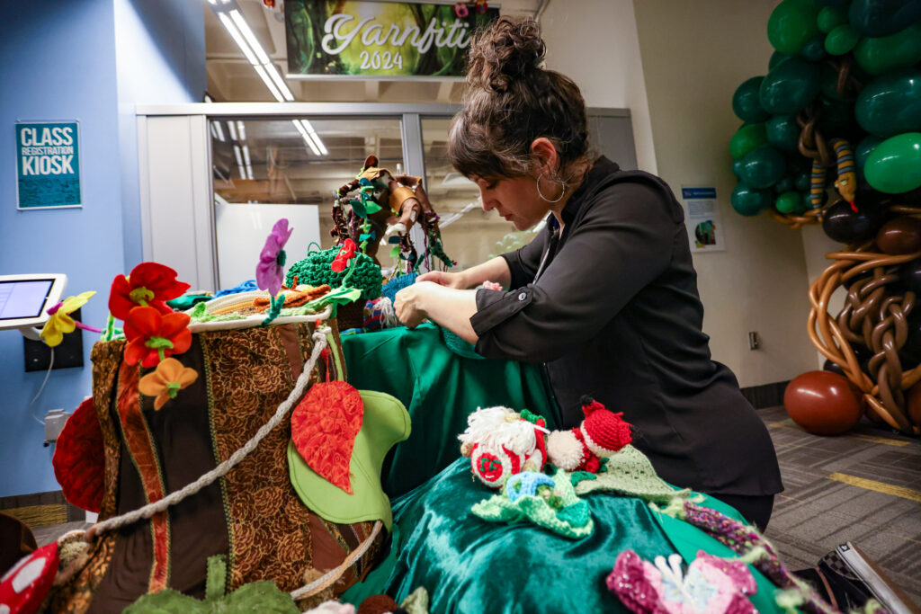 woman decorating a soft sculpture tree stump with green cloth and forest elements