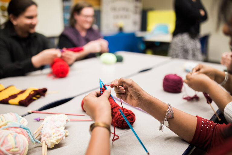 A group sitting around a table while all knitting