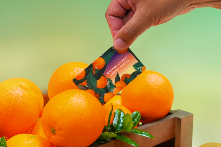 Hand pulling library card from a crate of oranges.