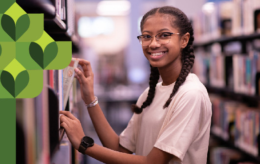 A teenage girl smiling while sifting through books on a shelf.