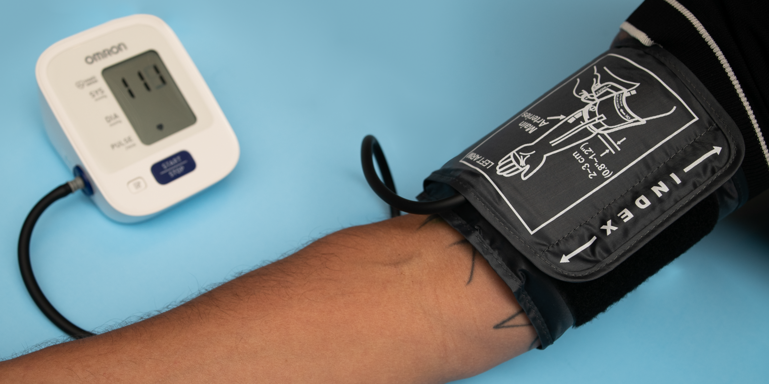 Photograph of a blood pressure monitor attached to a mans arm over a blue background.