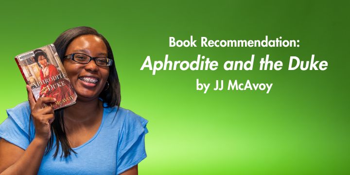 Woman holds book "Aphrodite and the Duke" next to her face in front of green background