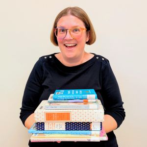 Smiling woman holds stack of books