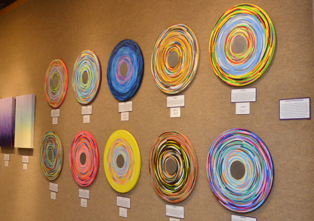 Circular color wheel paintings mounted on a wall for display.