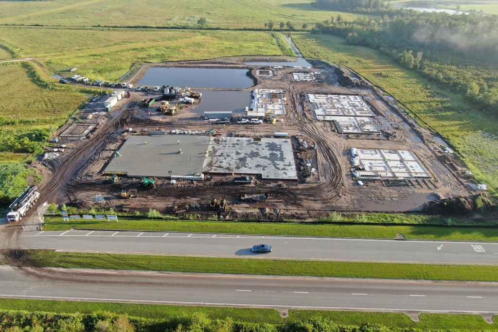 Aerial view of a construction site with multiple building foundations in progress, surrounded by green fields.