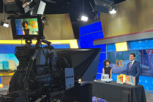 Youth Services Librarian in WESH studio behind table with props, shown on camera monitor