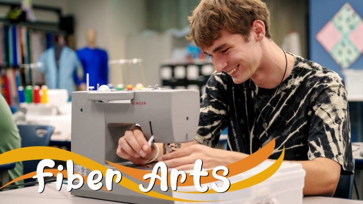A young man smiles as he uses a sewing machine. The text reads "Fiber Arts".