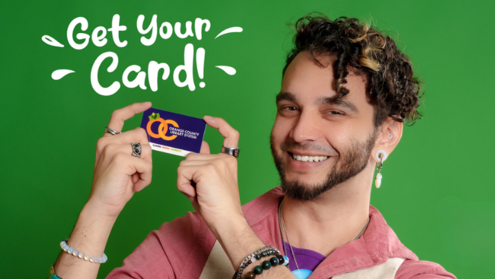 A young adult is smiling at the camera holding up their library card. The words "Get Your Card" are seen above them.