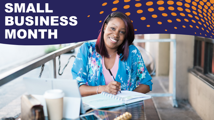 A woman smiles at the camera. She is sitting at a table outside with papers in front of her.