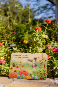 OCLS Florida pollinator library card propped up amidst flowers