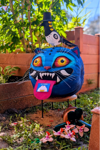 Pumpkin decorated as the KPop Demon Hunters character Derpy Tiger sits in garden with black and white bird perched on his head