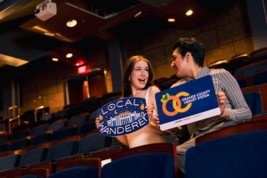 People in theater seating holding Local Wanderer and Orange County Library System oversized logos