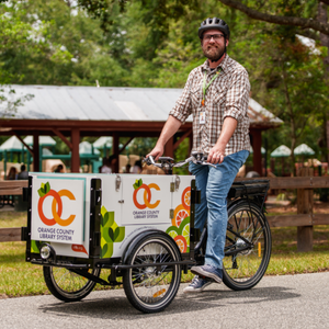 OCLS staff member Ethan rides the book bike