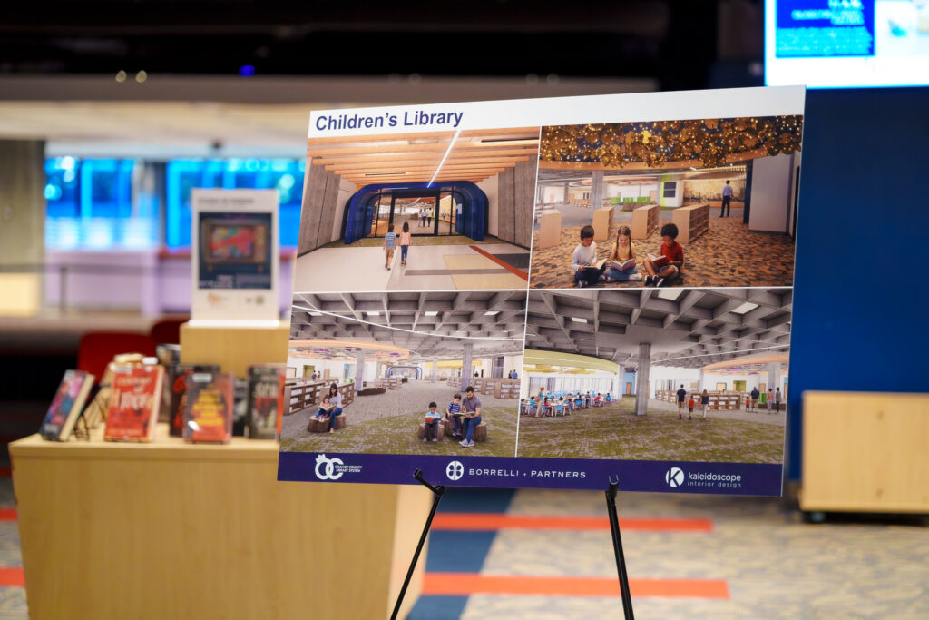 Easel-mounted presentation board titled “Children’s Library” featuring several architectural renderings of planned children's library spaces, including reading areas, bookshelves, and gathering spaces.