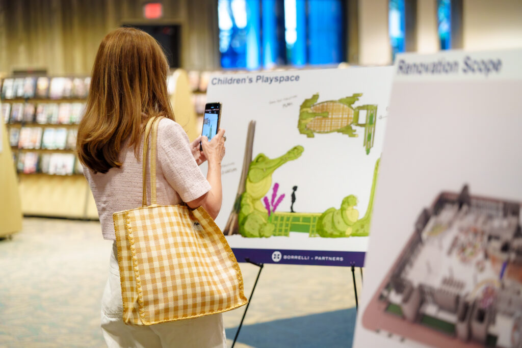 Visitor photographs a display board showing plans for a Children’s Playspace during the library’s first-floor renovation event.