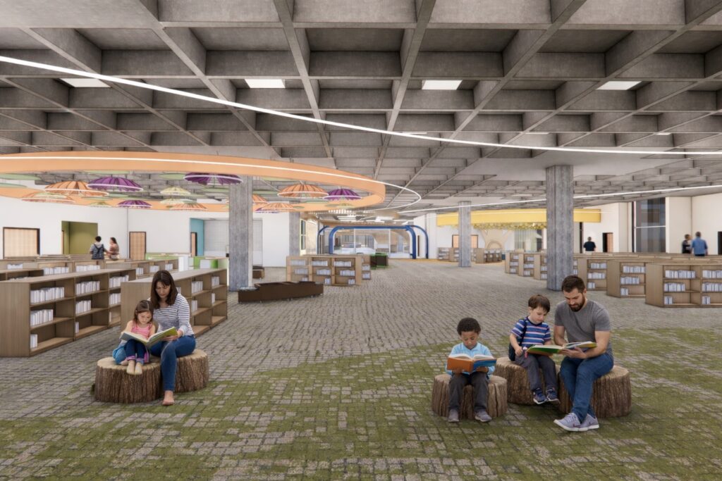 A large, open children’s library area with low bookshelves, tree‑stump seating, and a patterned floor, where several people sit and read; overhead, a grid ceiling and circular decorative elements add color and visual interest.