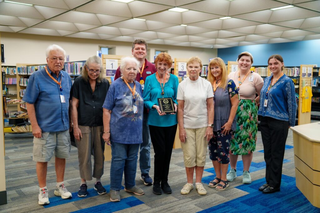 Friends of the Library volunteers stand with Sandi Trainor (holding plaque)
