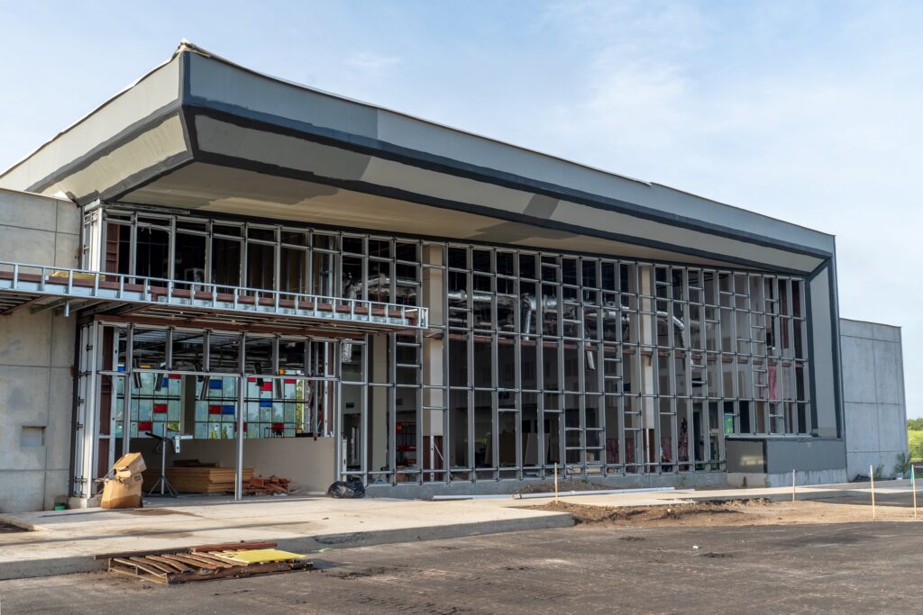 Close exterior view of a building under construction, showing exposed metal wall framing, visible ductwork, and an unfinished covered entrance.
