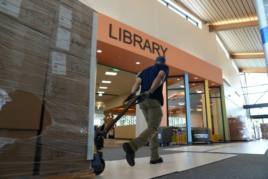 Worker transporting a pallet of boxed library materials through the library entrance during branch setup and stocking.