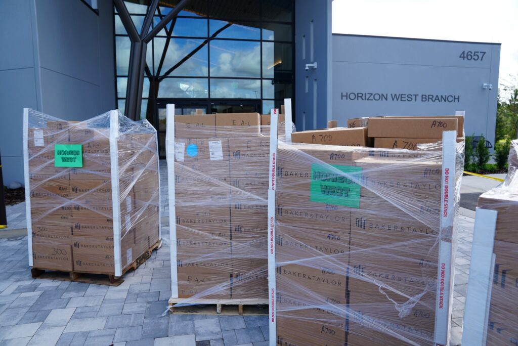 Shrink-wrapped pallets of boxed library materials staged outside the Horizon West Branch building before delivery and setup.