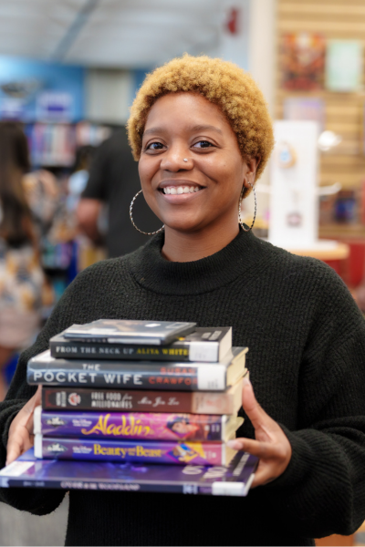 Jazmyne holds stack of books and movies in Friends of the Library bookstore