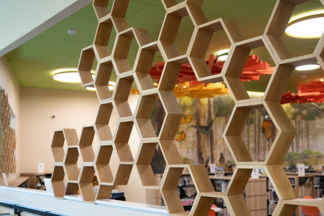 Close-up of honeycomb-shaped wooden dividers overlooking a colorful children’s library.